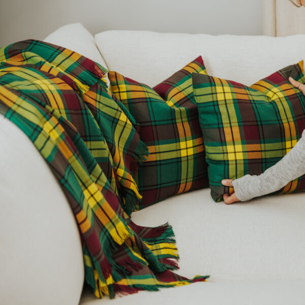 A woman is sitting on a couch with a Homespun Tartan Blanket/Throw.