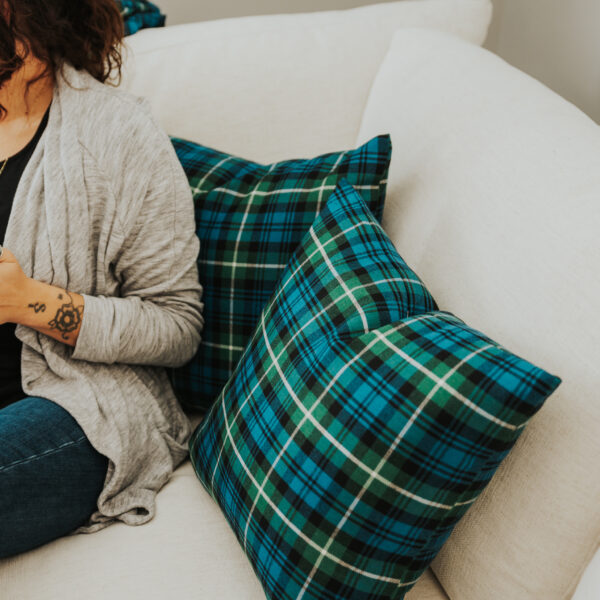 A woman sitting on a couch with Homespun Tartan Blanket/Throw pillows.