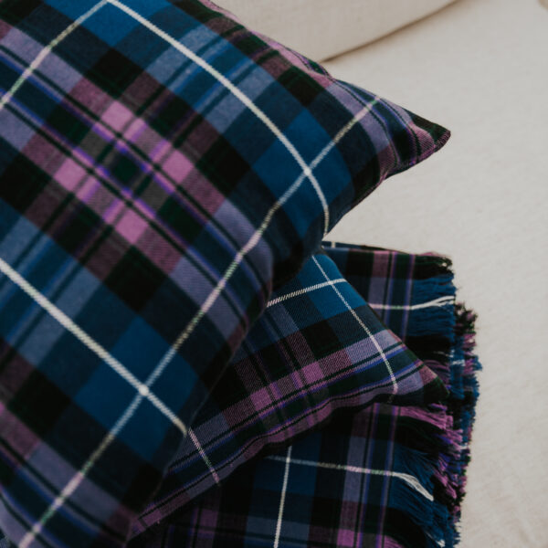 A blue and purple Homespun Tartan blanket/throw on a white couch.