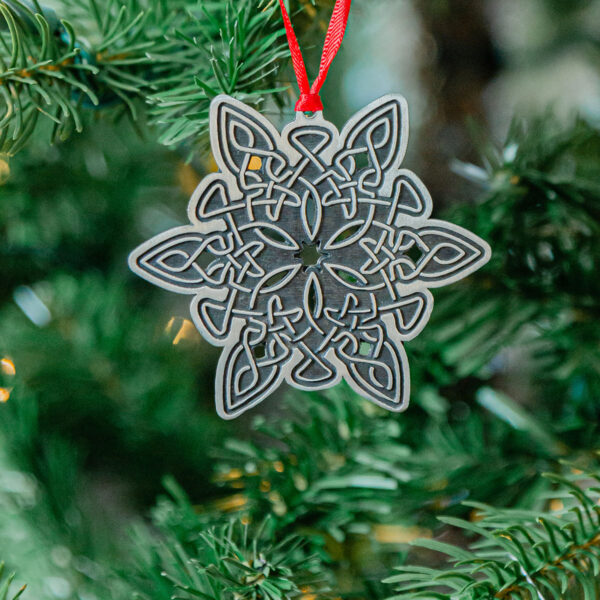 A celtic snowflake ornament hangs on a christmas tree.