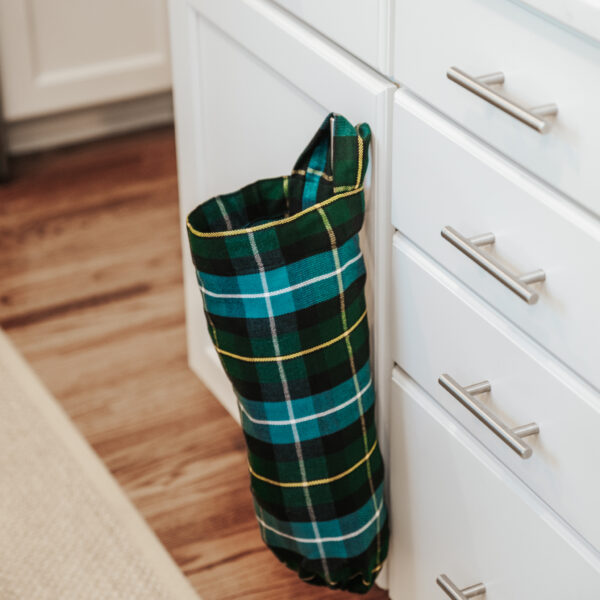 A Tartan Plastic Bag Holder - Homespun Wool Blend hanging on a kitchen cabinet.