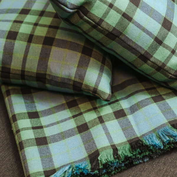 A green and black Homespun Tartan Blanket/Throw on top of a wooden table.