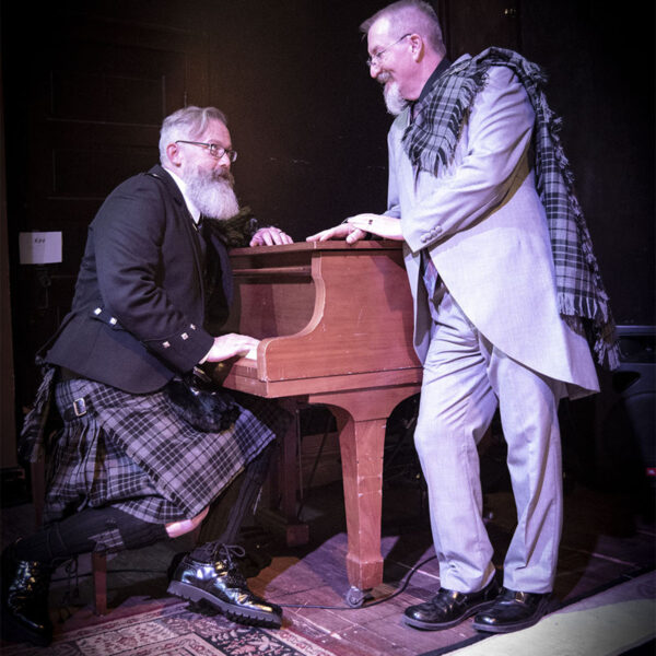 Two men in kilts standing next to a piano in the Argyle Formal PLATINUM Package.