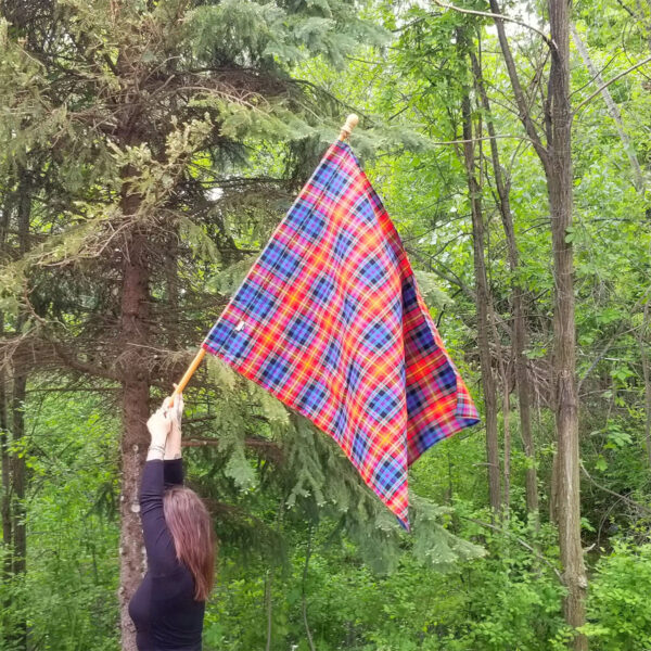 A woman is waving a LGBT Pride Tartan Flags - Homespun Wool Blend flag in the woods.
