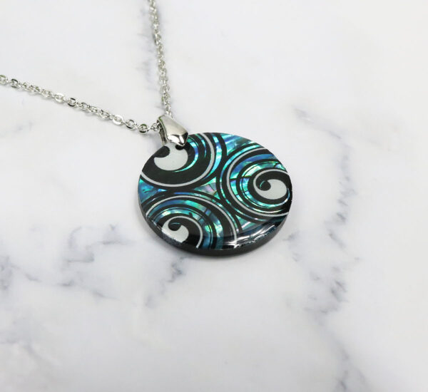 A Triskelion Spiral Paua Shell Necklace with a black and blue swirl design.