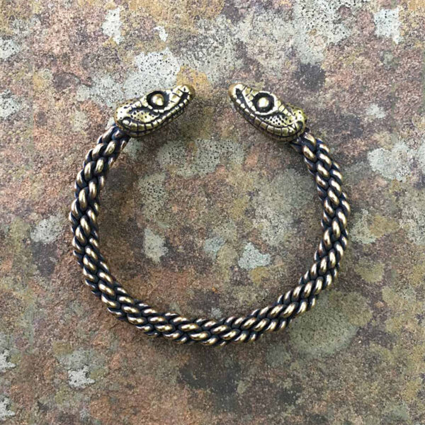 A Celtic Snake Torc Bracelet - Medium Braid with a black braided pattern resting on a stone surface.