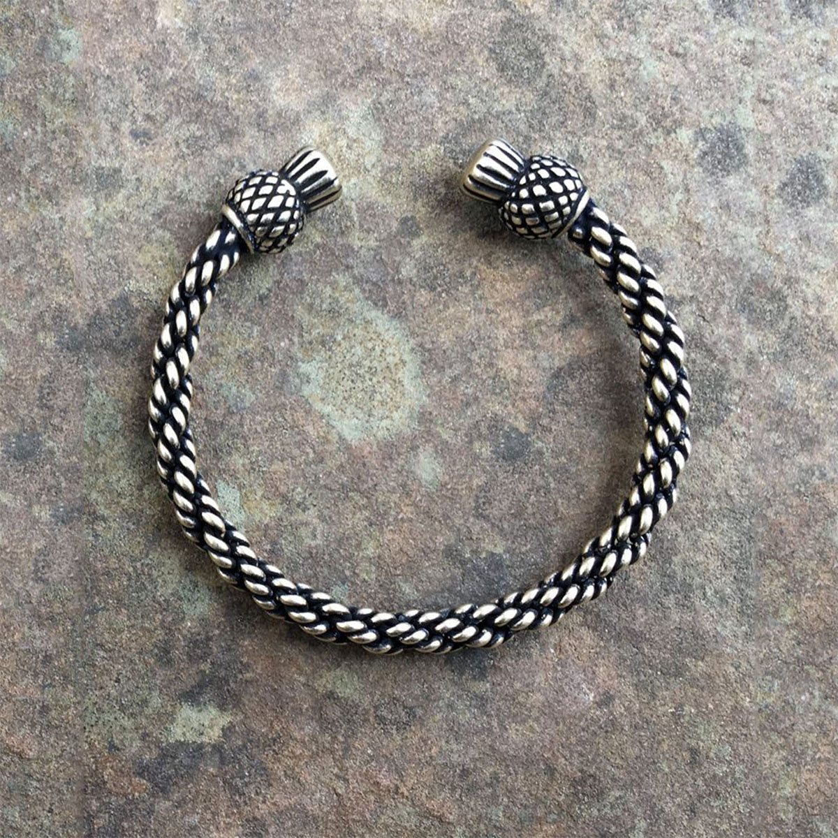 A black and white Celtic Thistle Torc Bracelet on a stone.