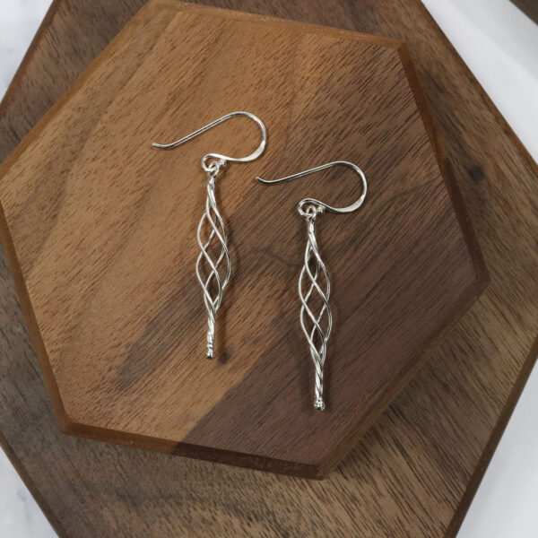 Triquetra Sterling Silver Earrings are resting on a wooden surface.