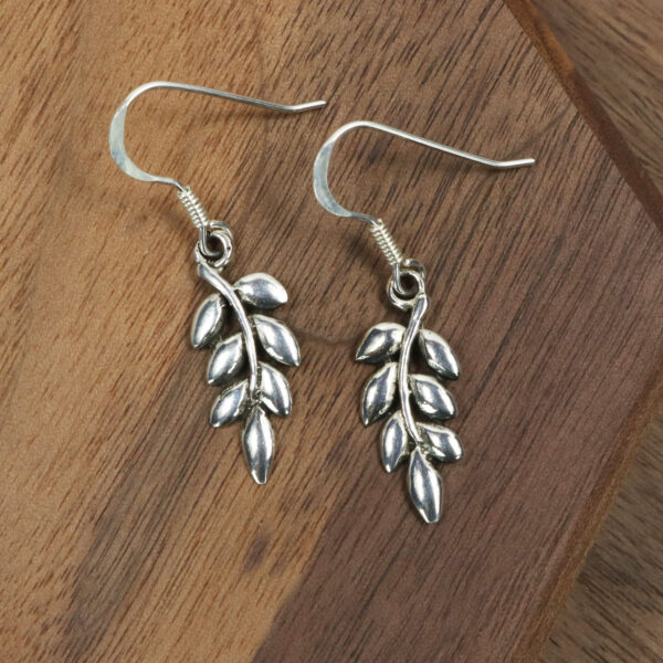 A pair of silver Ash Leaf Earrings made to resemble ash leaves, placed on a rustic wooden table.