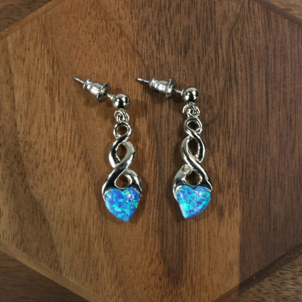 A pair of blue opal earrings on a wooden table, featuring Triquetra Sterling Silver Earrings.