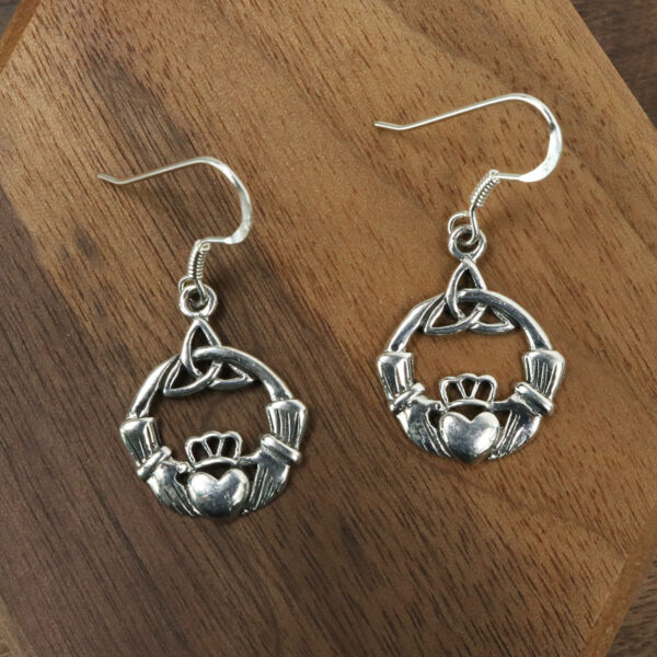 A pair of Sterling Silver Triquetra Claddagh Earrings on a wooden table.