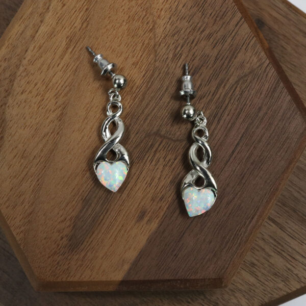 A pair of white opal earrings embellished with Triquetra Sterling Silver Earrings, gracefully displayed on a wooden table.