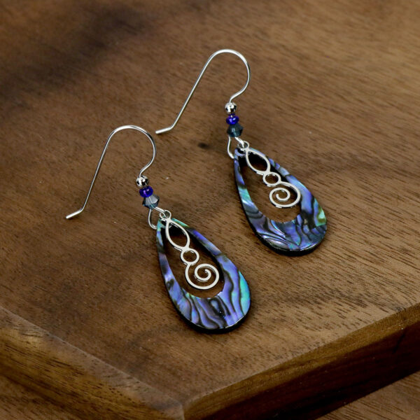 A pair of Celtic Spiral Paua Shell Earrings made of abalone shell on a wooden table.