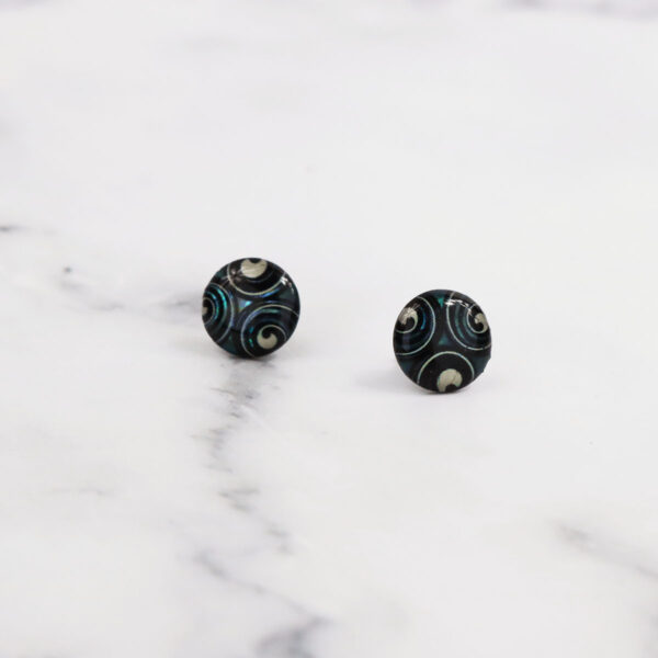 Triskelion Spiral Paua Shell Earrings on a marble surface.