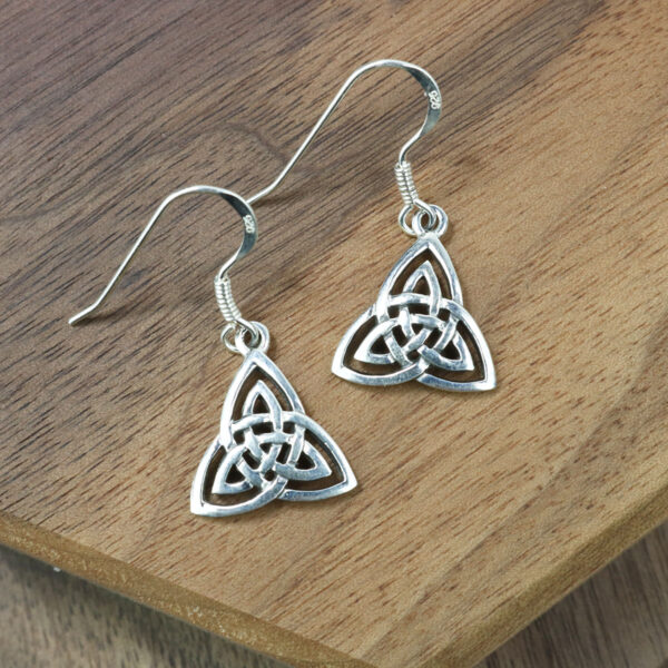 A pair of Trinity Knot Earrings on a wooden table.
