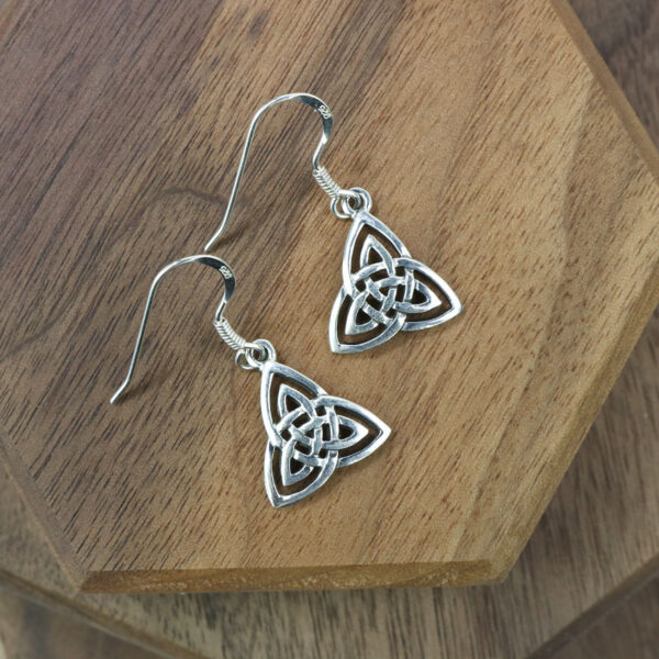 A pair of Trinity Knot Earrings made of sterling silver on a wooden table.