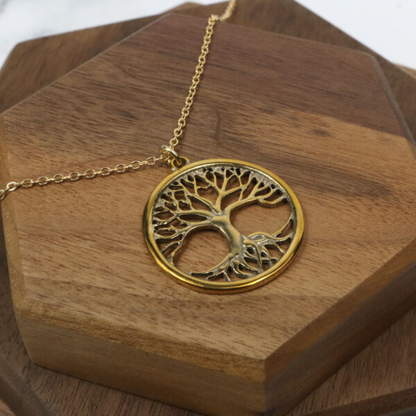 An Amethyst Celtic Knot Necklace with a gold tree of life pendant, adorned with an amethyst gemstone, on a wooden table.