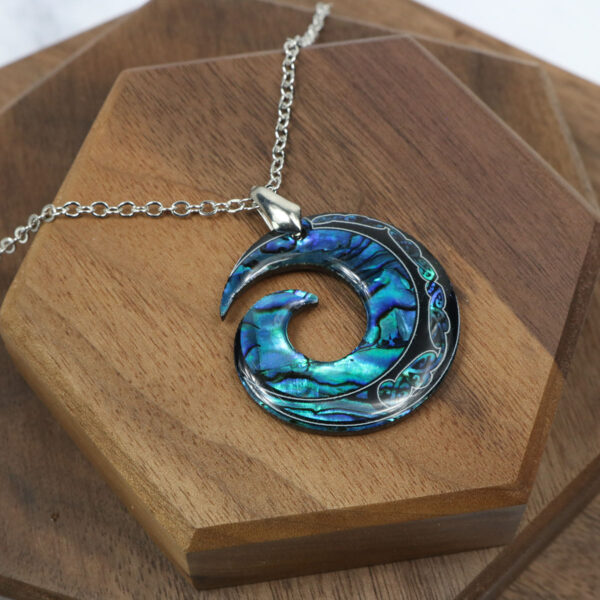 A Amethyst Celtic knot necklace with an abalone shell pendant resting on a wooden table.