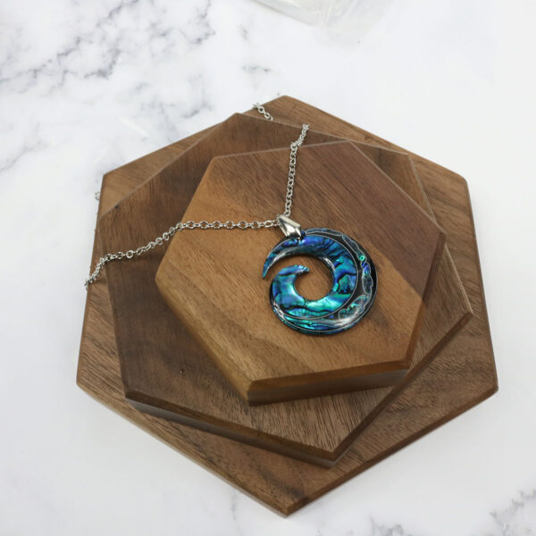 An Amethyst Celtic Knot Necklace with a blue abalone shell on top of a wooden board.
