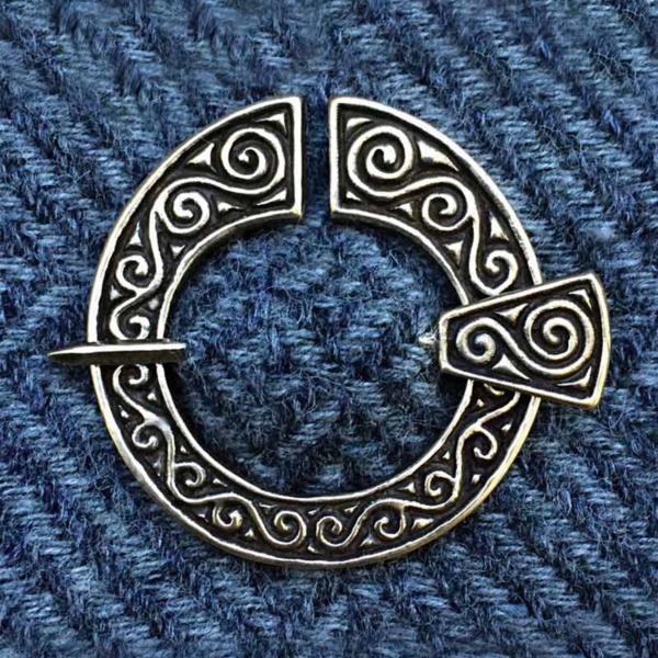 A silver celtic circle brooch on a blue cloth.