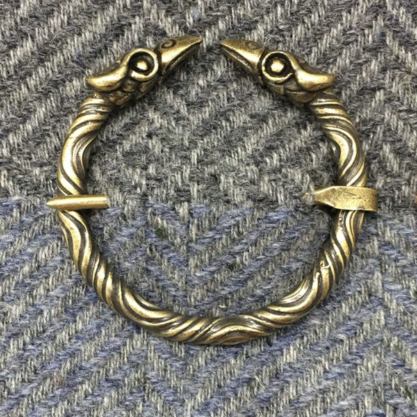 A brass Raven Penannular Brooch with a pair of eagles and a raven on it.