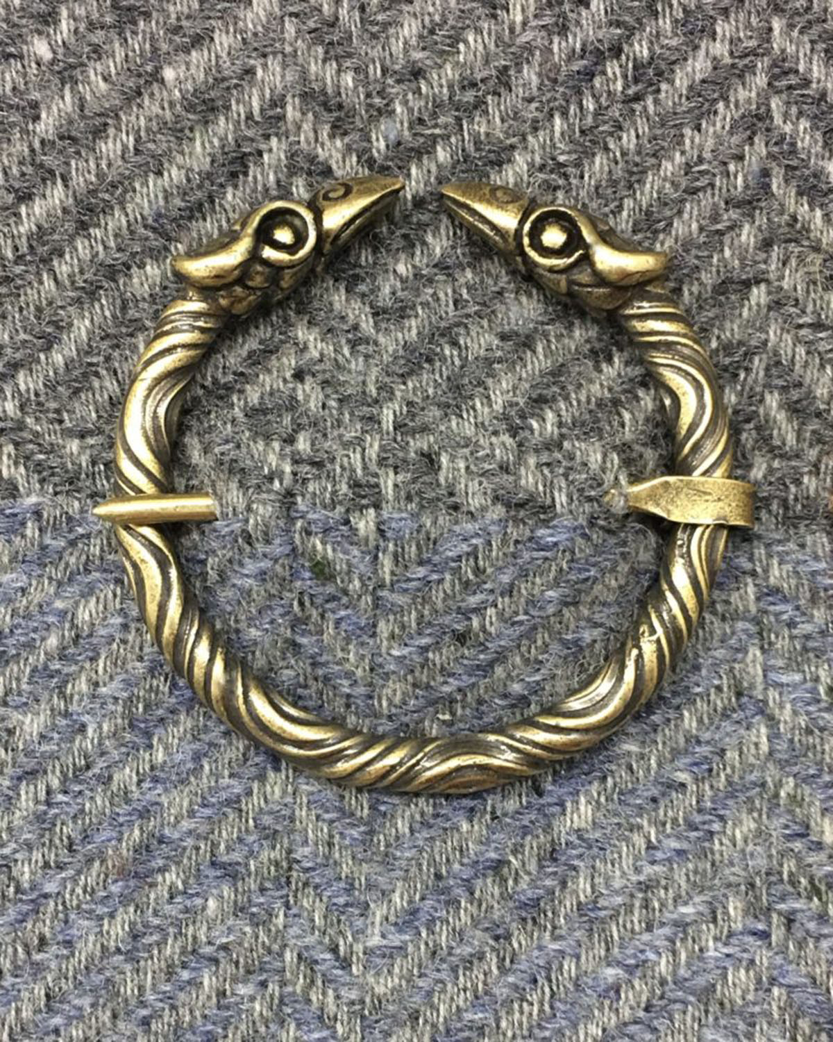 A brass Raven Penannular Brooch with a pair of eagles and a raven on it.