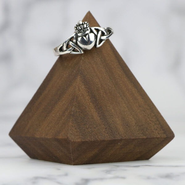 A silver claddagh ring with a Two Tone Eternity Knot Band resting on top of a wooden pyramid.
