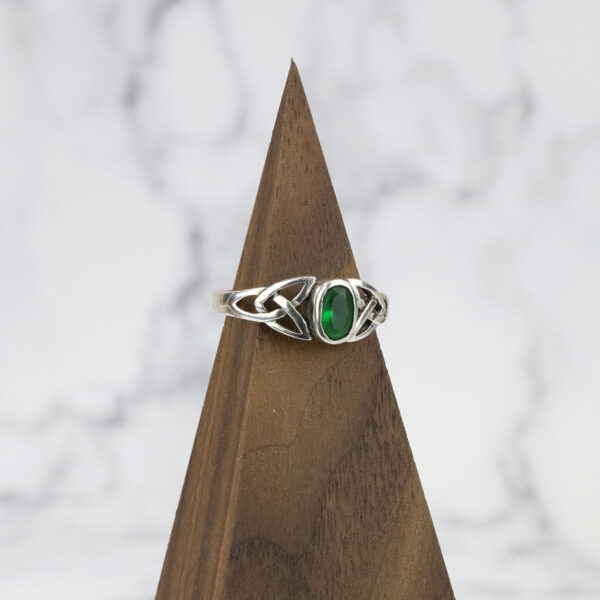 An emerald stone sits on top of a wooden base with a Two Tone Eternity Knot Band.
