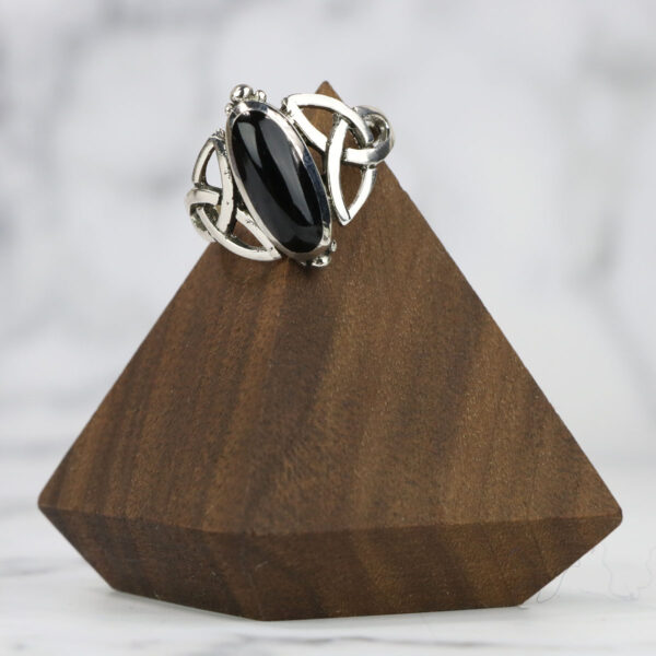 A Black Onyx Trinity Celtic Knot Ring on a wooden stand featuring a Trinity Celtic knot design.