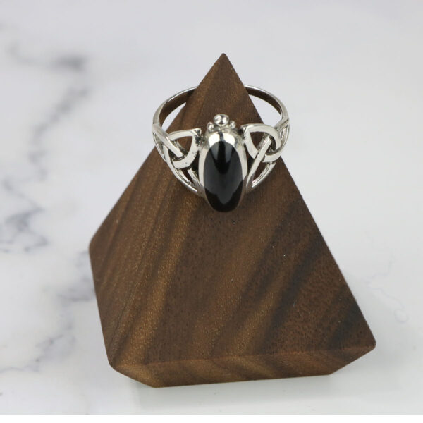 A Black Onyx Trinity Celtic Knot Ring on a wooden base adorned with the Celtic knot.