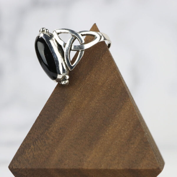 A Black Onyx Trinity Celtic Knot Ring featuring a trinity Celtic knot design, displayed on a sleek wooden stand.