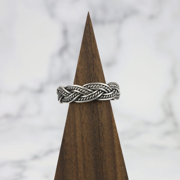 A Two Tone Eternity Knot Band with a braided pattern on top of a wooden base.