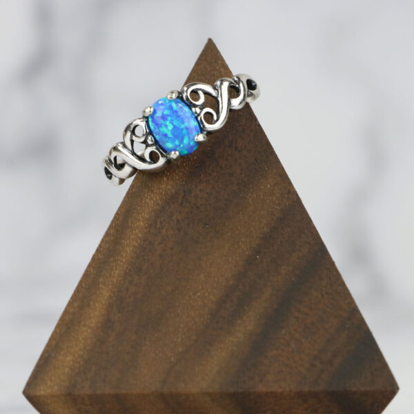 A Large Celtic Knot Spinner Ring with a blue opal on top of a wooden base.
