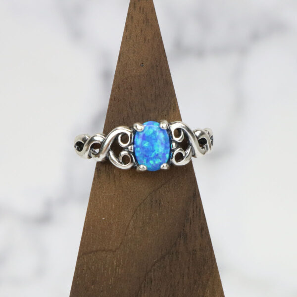 A Heart Knot Blue Opal Sterling Silver Ring on top of a wooden base.