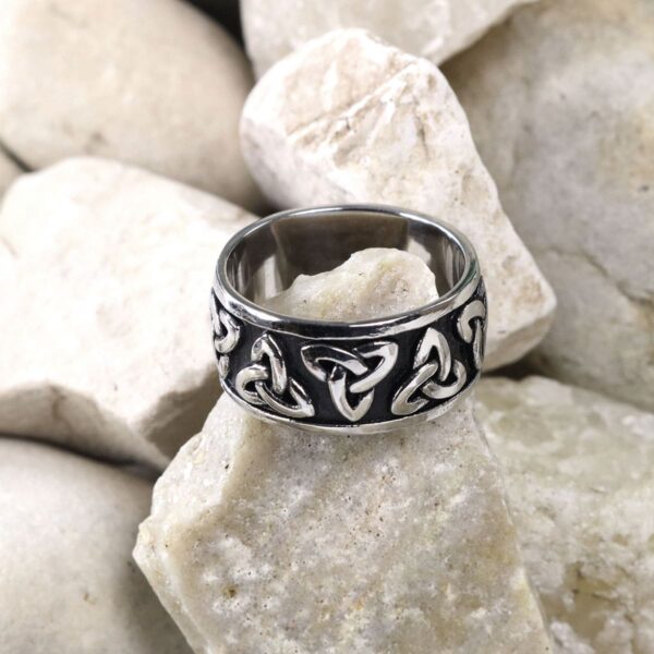 A Two Tone Triquetra Ring adorned with celtic knots atop rocks.