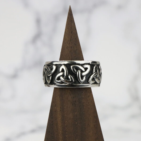 A Two Tone Triquetra Ring with celtic knots and triquetra design on top of a wooden base.