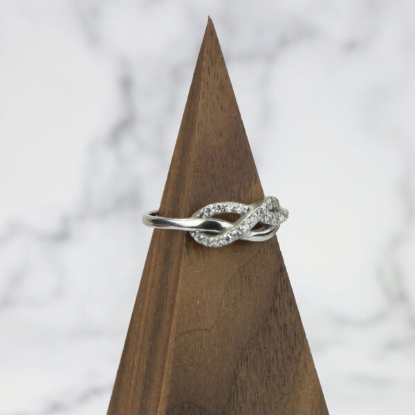 An Infinity Knot Ring with diamonds delicately placed on top of a sleek wooden base.