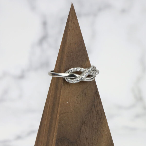 An Infinity Knot Ring with diamonds atop a wooden base.