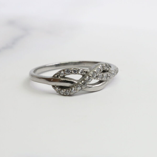 An Infinity Knot Ring with diamonds on a marble surface.