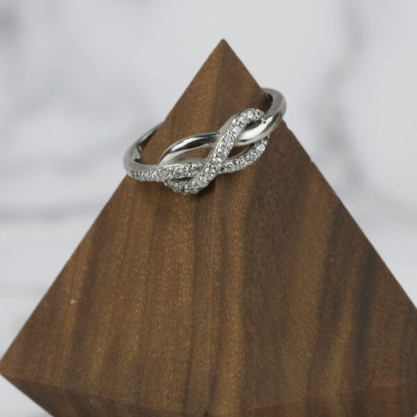 An Infinity Knot Ring with diamonds on top of a wooden block.