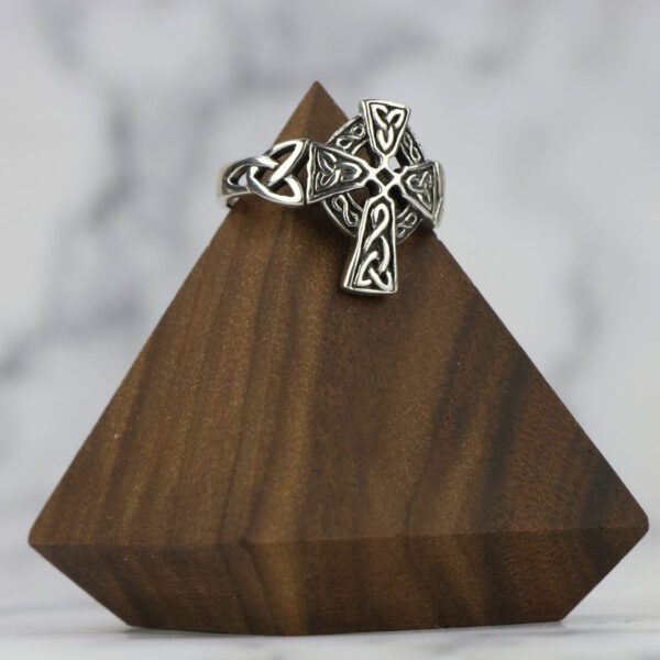 A silver celtic cross ring with a Two Tone Eternity Knot Band on a wooden stand.