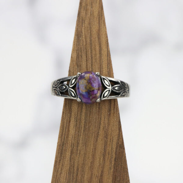 A Purple Mohave Turquoise Triquetra ring on a wooden base.