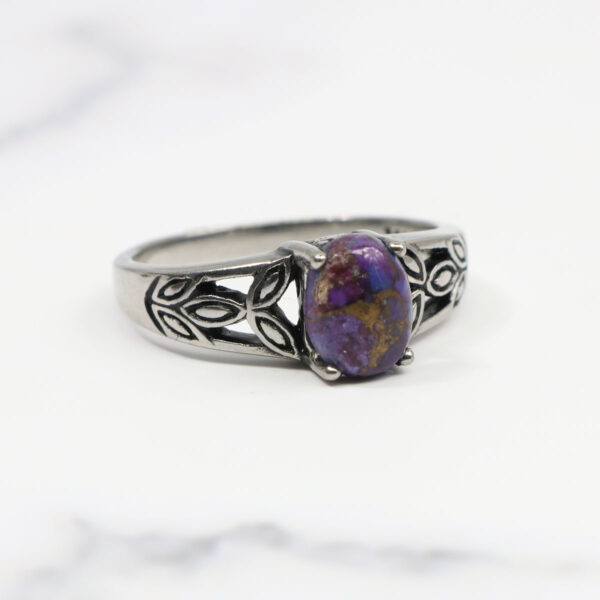 A Purple Mohave Turquoise Triquetra Ring sits majestically on a marble table, showcasing its brilliant colors.