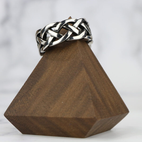An Interlacing Endless Knot Ring displayed on a simple wooden stand.