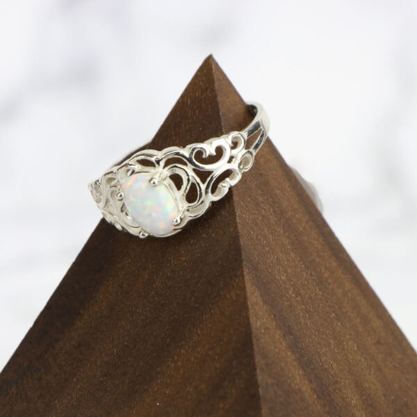 A white opal ring with a Two Tone Eternity Knot Band and a filigree design.