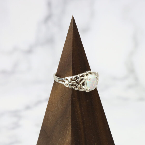 A white opal ring with a Two Tone Eternity Knot Band on top of a wooden pedestal.