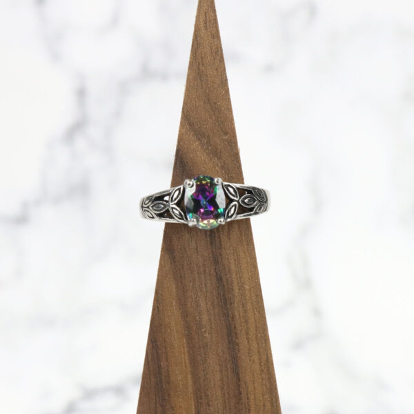 A Mystic Crystal Stainless Steel Ring with a rainbow colored stone on top of a wooden base.