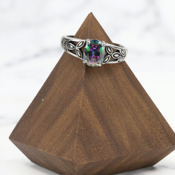 A Mystic Crystal Stainless Steel Ring with a multi colored stone on top of a wooden base.