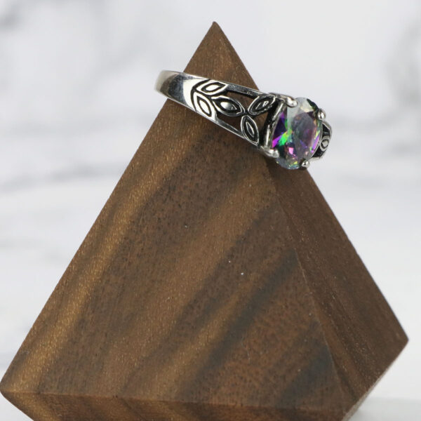 A Mystic Crystal Stainless Steel Ring with a rainbow colored stone atop a wooden block.