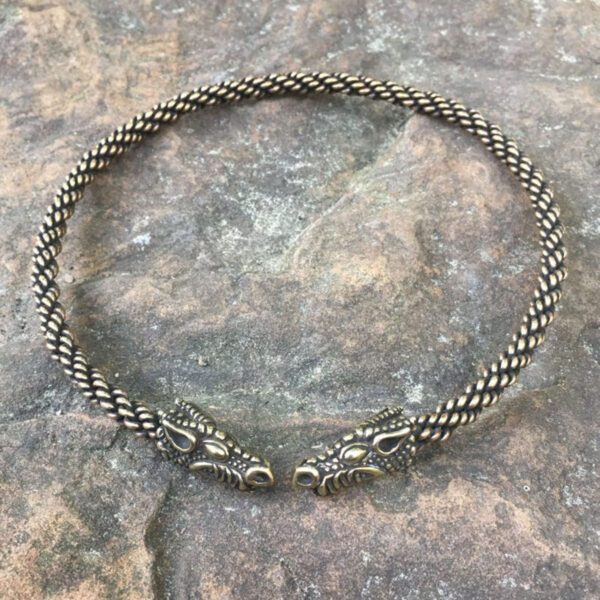 A Celtic Dragon Neck Torc with two dragon heads on top of a stone.